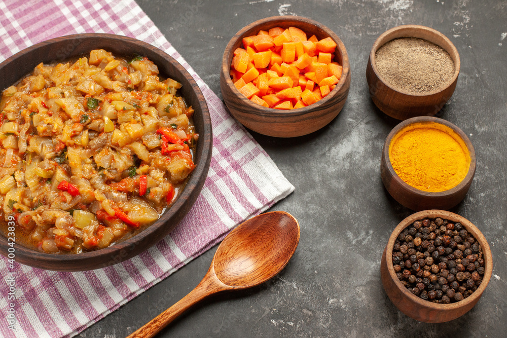 top view roasted eggplant salad in bowl bowls with different spices cuts cubs of carrot wooden spoon on dark background top view roasted eggplant salad in bowl bowls with different spices cuts cubs of carrot wooden spoon on dark background