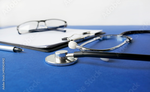 Medical stethoscope and clipboard with a blank sheet of paper on a blue background. View from above. Medical concept.