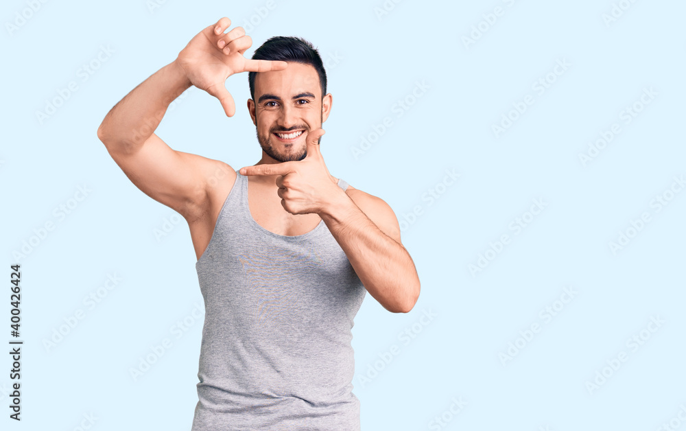 Young handsome man wearing swimwear and sleeveless t-shirt smiling making frame with hands and fingers with happy face. creativity and photography concept. Young handsome man wearing swimwear and sleeveless t-shirt smiling making frame with hands and fingers with happy face. creativity and photography concept.