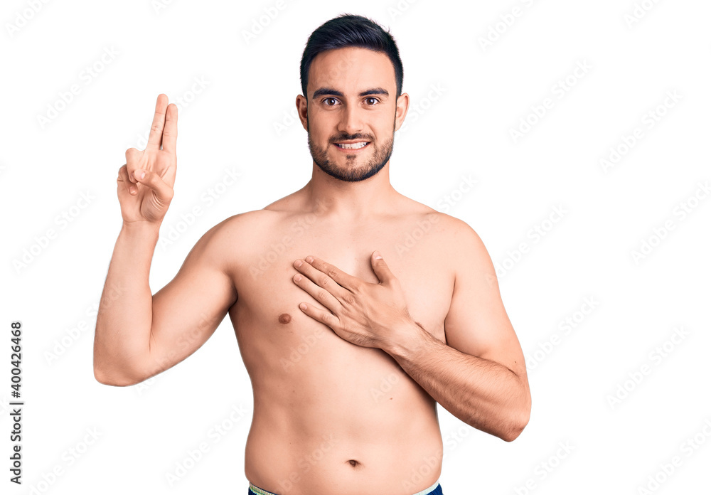 Fototapeta premium Young handsome man wearing swimwear smiling swearing with hand on chest and fingers up, making a loyalty promise oath