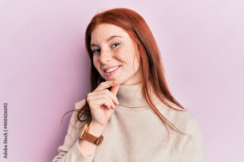 Young red head girl wearing turtleneck sweater smiling looking confident at the camera with crossed arms and hand on chin. thinking positive. Young red head girl wearing turtleneck sweater smiling looking confident at the camera with crossed arms and hand on chin. thinking positive.