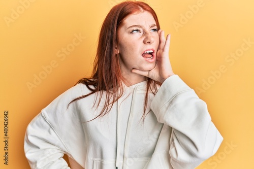 Young red head girl wearing casual sweatshirt shouting and screaming loud to side with hand on mouth. communication concept.