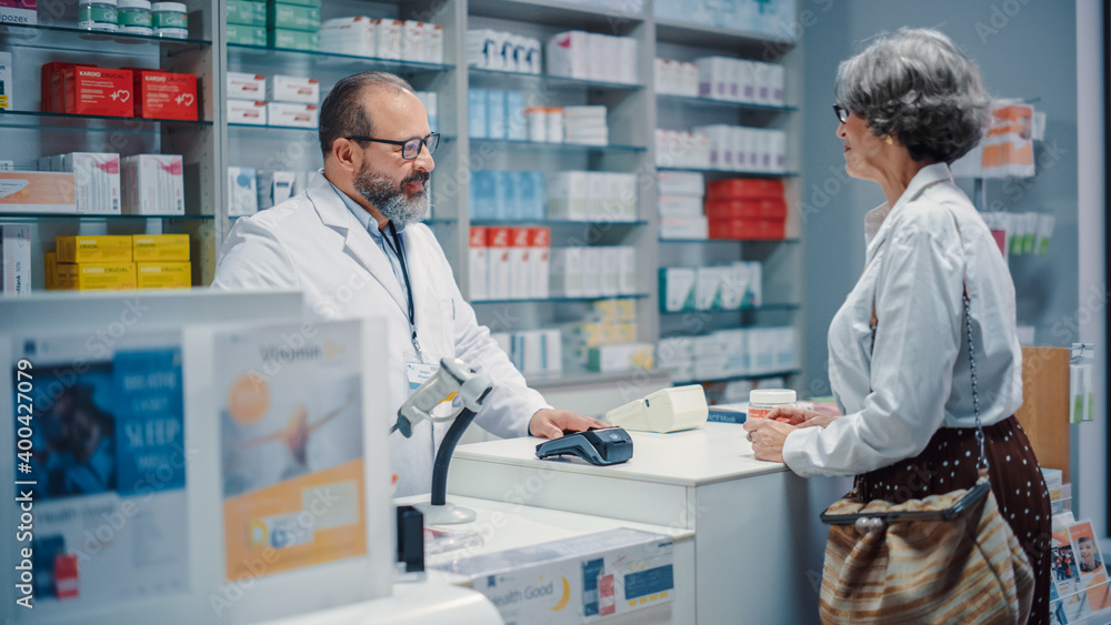 Pharmacy Drugstore Checkout Cashier Counter: Portrait of Friendly Pharmacist Recommending Medicine to Senior Woman which She buys Using Contactless Payment Credit Card. Store with Health Care Products Pharmacy Drugstore Checkout Cashier Counter: Portrait of Friendly Pharmacist Recommending Medicine to Senior Woman which She buys Using Contactless Payment Credit Card. Store with Health Care Products