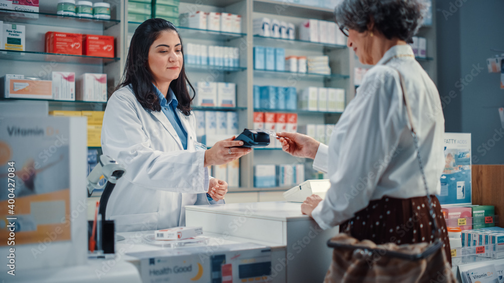 Pharmacy Drugstore Checkout Cashier Counter: Beautiful Female Pharmacist and Senior Woman Using Contactless Payment Credit Card to Buy Prescription Medicine, Vitamins, Health Care Products