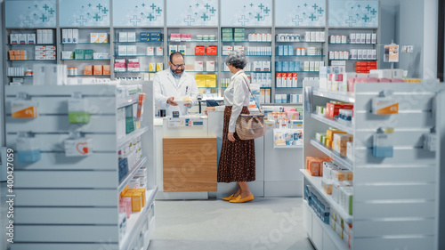 Pharmacy Drugstore Checkout Cashier Counter: Senior Woman Buying Prescription Medicine, Drugs, Vitamins and Talks to Beautiful Pharmacist Cashier, Asking Recomendations. Store with Health Care Goods photo