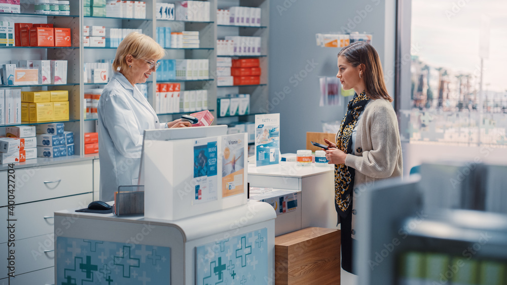 Obraz premium Pharmacy Drugstore Checkout Cashier Counter: Mature Female Pharmacist and Young Woman Using Contactless Payment NFC Smartphone to Buy Prescription Medicine, Vitamins, Beauty, Health Care Products