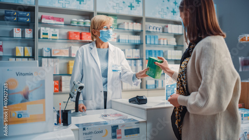 Pharmacy Drugstore Checkout Cashier Counter: Pharmacist and Young Woman Using Contactless Payment Credit Card to Buy Prescription Medicine, Vitamins. People Wearing Protective Face Masks photo