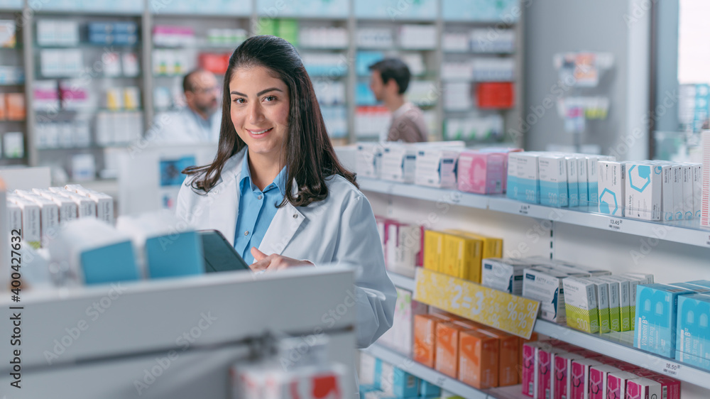 Pharmacy Drugstore: Portrait Shot of Beautiful Latina Pharmacist Wearing White Coat, Standing Among Shelfs with Health Care Products and Looks at the Camera, Smiles Charmingly. Professional Pharmacist