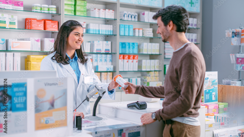 Pharmacy Drugstore Checkout Cashier Counter: Beautiful Latin Female Pharmacist Passes Box of Vitamins to a Young Male Customer. He is Buying Prescription Medicine, Vitamins, Health Care Products.