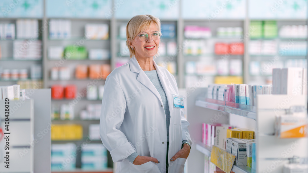 Pharmacy Drugstore: Portrait of Beautiful Professional Mature Caucasian Female Pharmacist Stands Among Shelfs with Medicines and Looks at the Camera, Smiles Charmingly. Store with Health Care Products