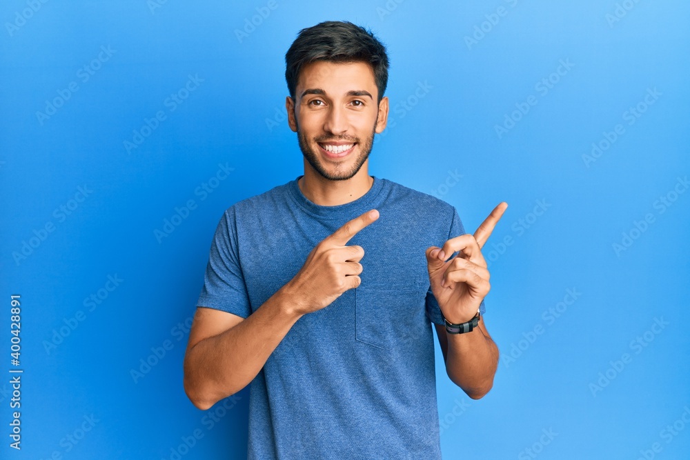 Young handsome man wearing casual tshirt over blue background smiling and looking at the camera pointing with two hands and fingers to the side. Young handsome man wearing casual tshirt over blue background smiling and looking at the camera pointing with two hands and fingers to the side.