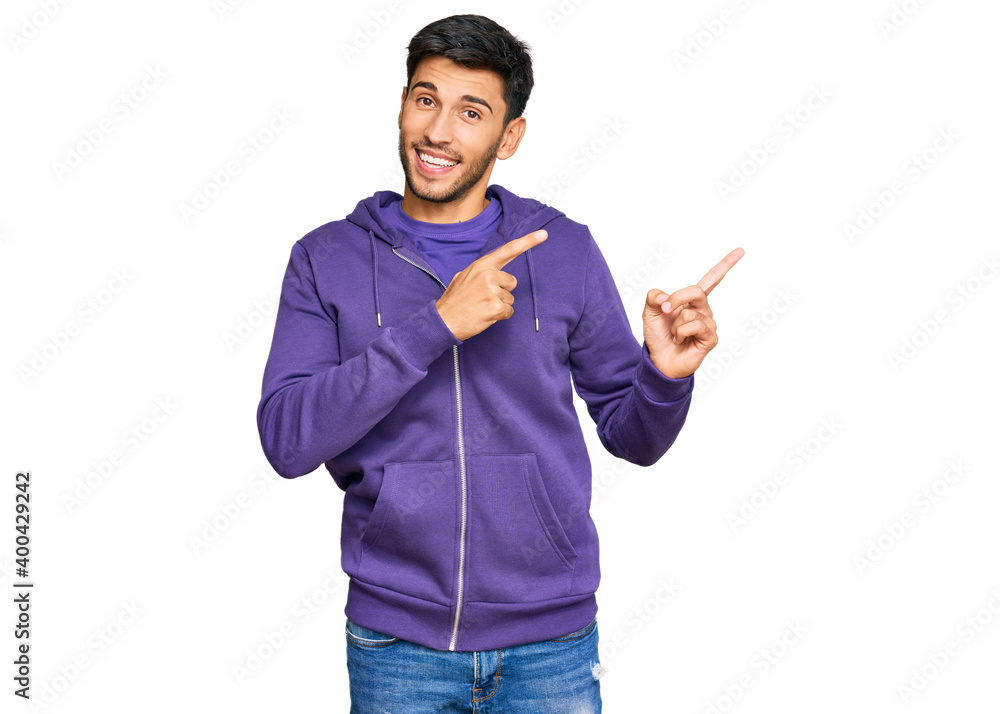 Young handsome man wearing casual sweatshirt smiling and looking at the camera pointing with two hands and fingers to the side. Young handsome man wearing casual sweatshirt smiling and looking at the camera pointing with two hands and fingers to the side.