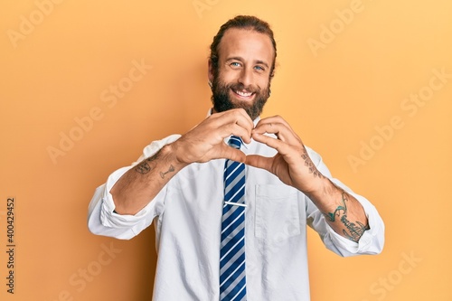Handsome man with beard and long hair wearing business clothes smiling in love doing heart symbol shape with hands. romantic concept.