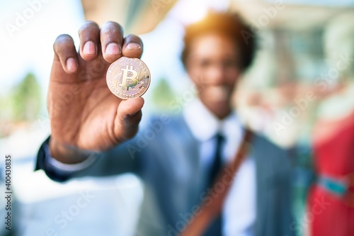 Young handsome african american businessman wearing suit smiling happy. Standing with smile on face holding bitcoin at town street.