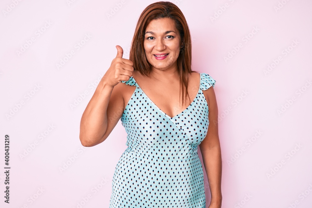 Middle age brunette hispanic woman wearing summer dress smiling happy and positive, thumb up doing excellent and approval sign Middle age brunette hispanic woman wearing summer dress smiling happy and positive, thumb up doing excellent and approval sign