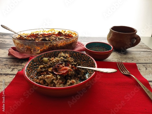 Baked quinoa with lentils, sliced tomatoes and chards. Red bowl of quinoa in a suthern mediterranean style and red tablecloth photo