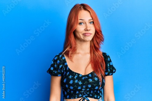 Young beautiful redhead woman wearing casual clothes over blue background looking sleepy and tired, exhausted for fatigue and hangover, lazy eyes in the morning.
