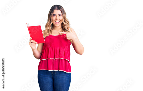 Young caucasian woman holding book smiling happy pointing with hand and finger