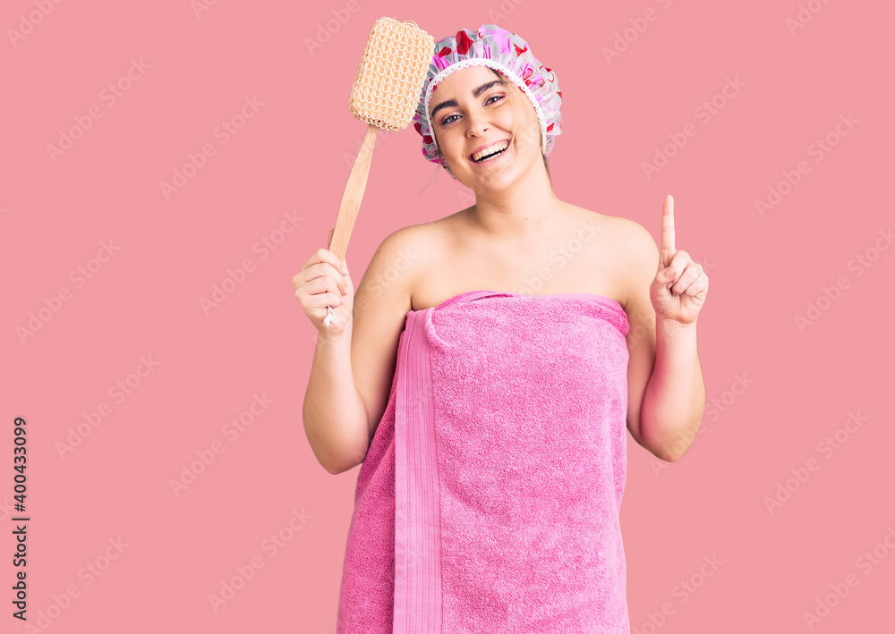 Young caucasian woman wearing shower cap and towel holding sponge surprised with an idea or question pointing finger with happy face, number one Young caucasian woman wearing shower cap and towel holding sponge surprised with an idea or question pointing finger with happy face, number one