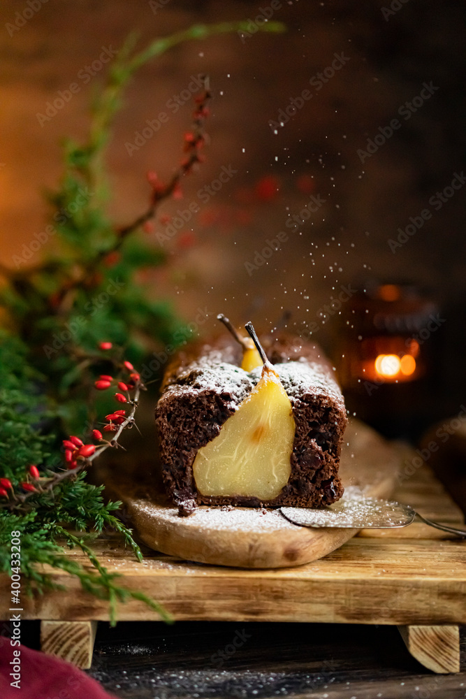 Chocolate pear sponge cake with whole fruits, wooden rustic table. Pear pie with christmas tree brush, candle. Winter homemade dessert. Copy space, selective focus.