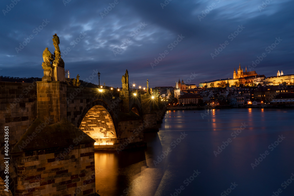 Fototapeta premium old illuminated prague castle and charles bridge and st. vita church lights from street lights are reflected on the surface of the vltava river in the center of prague at night in the czech republic