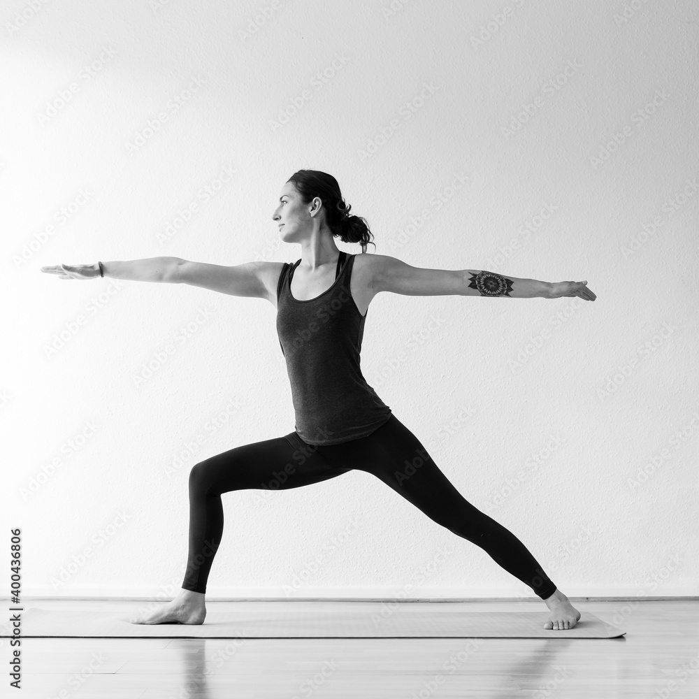 Fototapeta premium A brunette European woman in her 30’s practices yoga at home. Meditation, stretching and mindfulness to achieve physical and spiritual health. Black and white square format