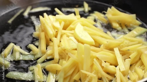 chef puts many small slices of yukon gold potatoes into a frying pan. finely chopped vegetable, butter or oil boils and bubbles close-up photo