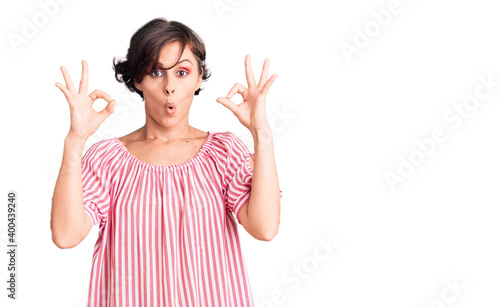 Beautiful young woman with short hair wearing casual summer clothes looking surprised and shocked doing ok approval symbol with fingers. crazy expression