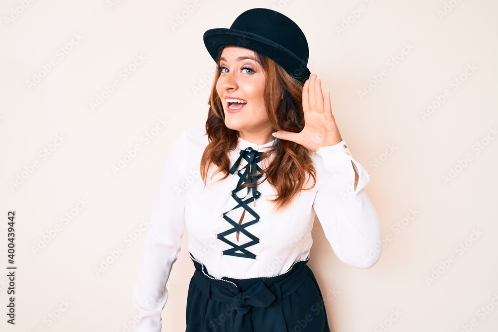 Young beautiful caucasian woman wearing elegant style and hat smiling with hand over ear listening and hearing to rumor or gossip. deafness concept. Young beautiful caucasian woman wearing elegant style and hat smiling with hand over ear listening and hearing to rumor or gossip. deafness concept.