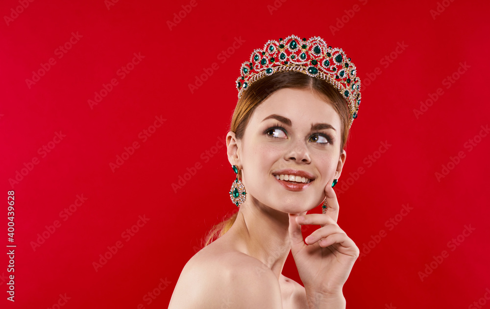 Portrait of a confident woman on a red background with a crown on her head and earrings on her ears Portrait of a confident woman on a red background with a crown on her head and earrings on her ears