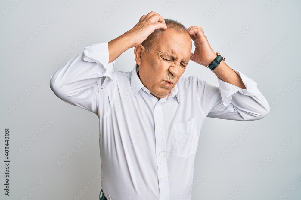 Handsome senior man wearing casual white shirt suffering from headache desperate and stressed because pain and migraine. hands on head. Handsome senior man wearing casual white shirt suffering from headache desperate and stressed because pain and migraine. hands on head.
