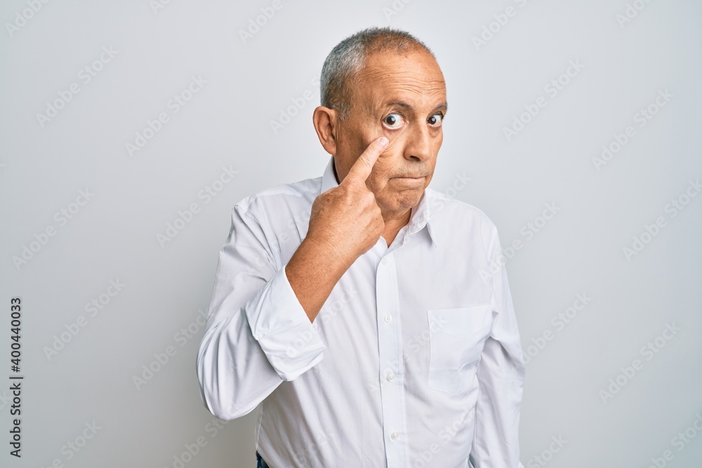 Handsome senior man wearing casual white shirt pointing to the eye watching you gesture, suspicious expression
