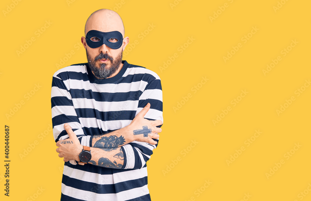 Young handsome man wearing burglar mask shaking and freezing for winter cold with sad and shock expression on face Young handsome man wearing burglar mask shaking and freezing for winter cold with sad and shock expression on face