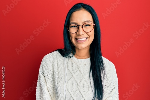 Beautiful hispanic woman wearing casual sweater and glasses looking positive and happy standing and smiling with a confident smile showing teeth