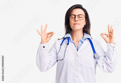 Young beautiful woman wearing doctor stethoscope and glasses relax and smiling with eyes closed doing meditation gesture with fingers. yoga concept.