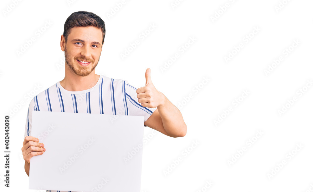 Handsome young man with bear holding blank empty banner smiling happy and positive, thumb up doing excellent and approval sign Handsome young man with bear holding blank empty banner smiling happy and positive, thumb up doing excellent and approval sign