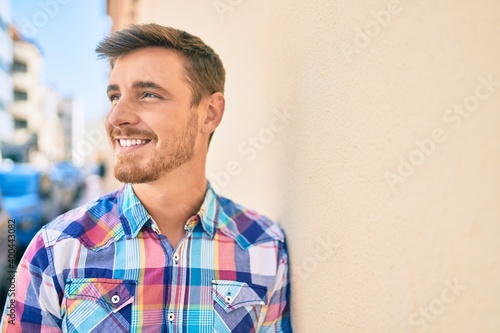 Young caucasian man smiling happy leaning on the wall at the city.