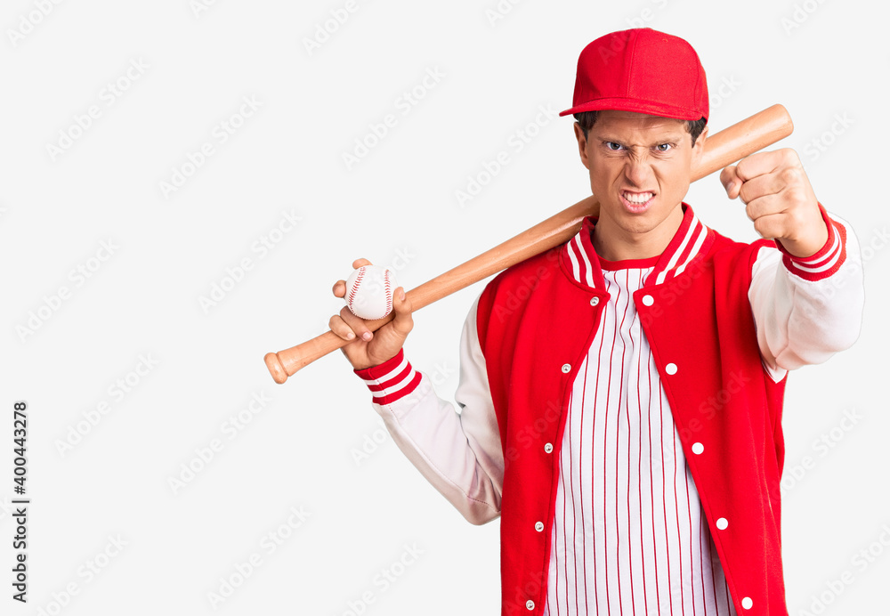Young handsome man playing baseball holding bat and ball annoyed and frustrated shouting with anger, yelling crazy with anger and hand raised Young handsome man playing baseball holding bat and ball annoyed and frustrated shouting with anger, yelling crazy with anger and hand raised