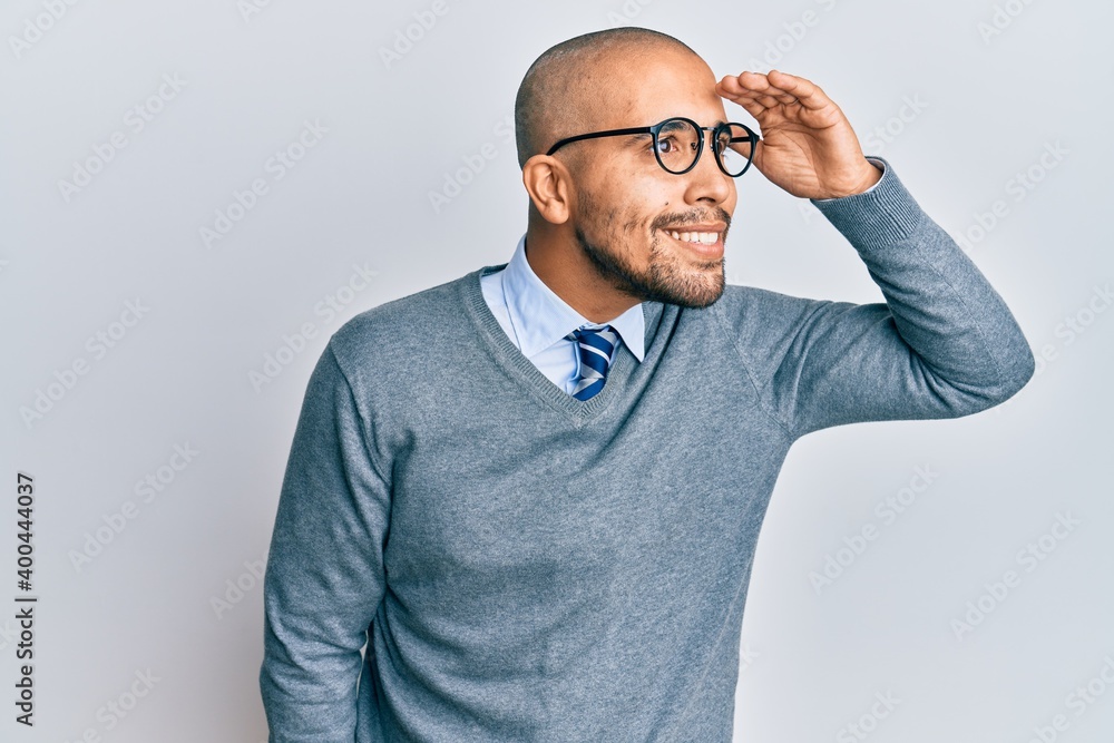 Hispanic adult man wearing glasses and business style very happy and smiling looking far away with hand over head. searching concept. Hispanic adult man wearing glasses and business style very happy and smiling looking far away with hand over head. searching concept.
