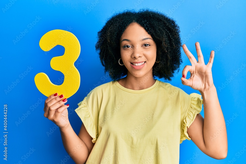 Young african american girl holding number three doing ok sign with fingers, smiling friendly gesturing excellent symbol Young african american girl holding number three doing ok sign with fingers, smiling friendly gesturing excellent symbol