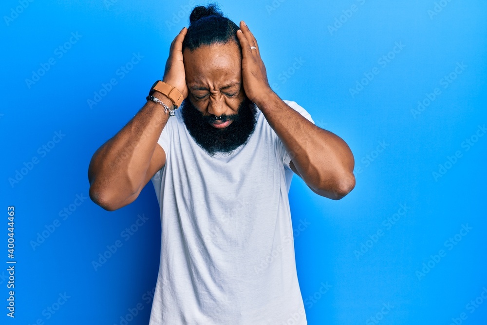 Young african american man wearing casual white tshirt suffering from headache desperate and stressed because pain and migraine. hands on head. Young african american man wearing casual white tshirt suffering from headache desperate and stressed because pain and migraine. hands on head.