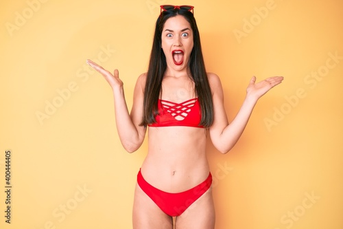 Young beautiful caucasian woman wearing bikini celebrating victory with happy smile and winner expression with raised hands