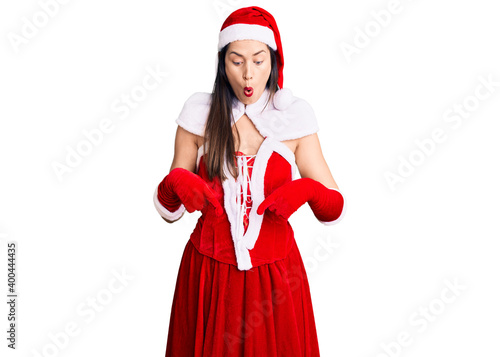 Young beautiful caucasian woman wearing santa claus costume pointing down with fingers showing advertisement, surprised face and open mouth
