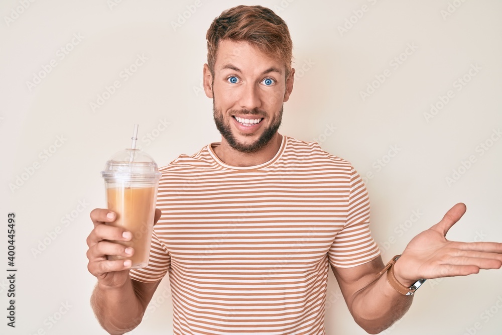Young caucasian man drinking glass of orange juice celebrating achievement with happy smile and winner expression with raised hand Young caucasian man drinking glass of orange juice celebrating achievement with happy smile and winner expression with raised hand