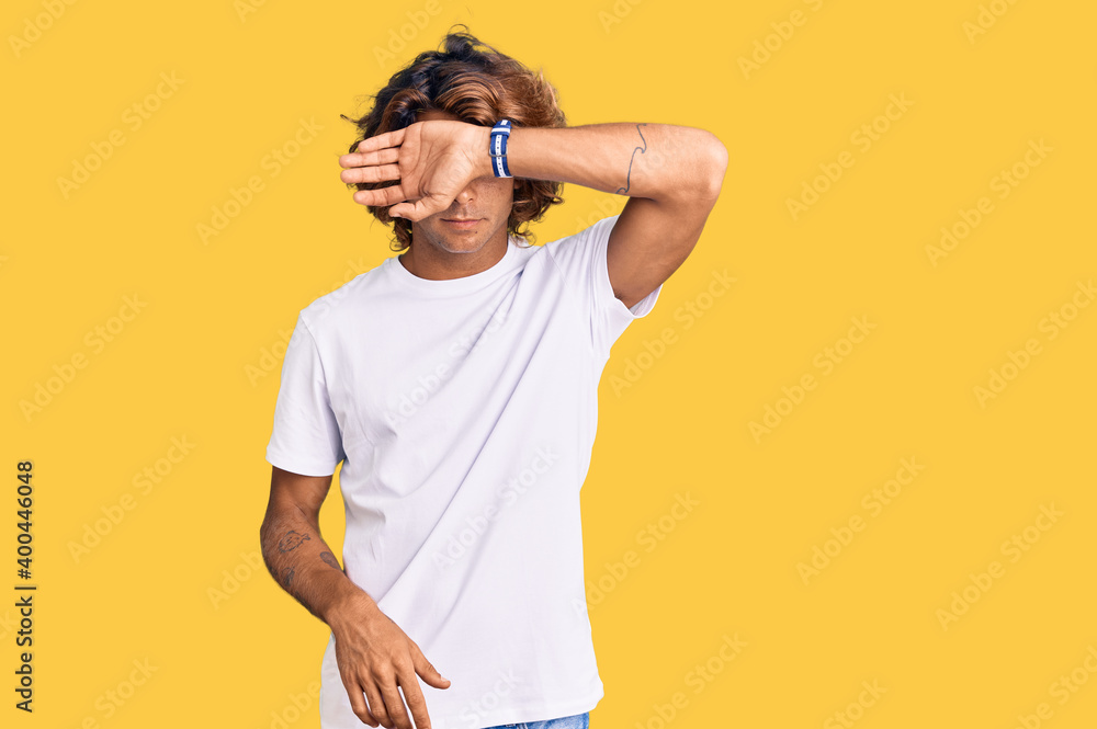 Young hispanic man wearing casual white tshirt covering eyes with arm, looking serious and sad. sightless, hiding and rejection concept Young hispanic man wearing casual white tshirt covering eyes with arm, looking serious and sad. sightless, hiding and rejection concept