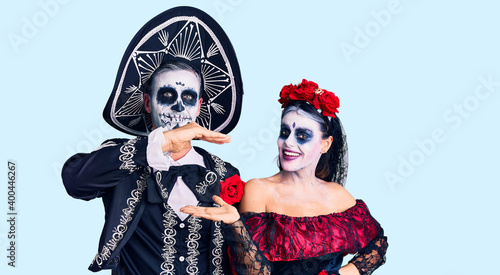Young couple wearing mexican day of the dead costume over background gesturing with hands showing big and large size sign, measure symbol. smiling looking at the camera. measuring concept.