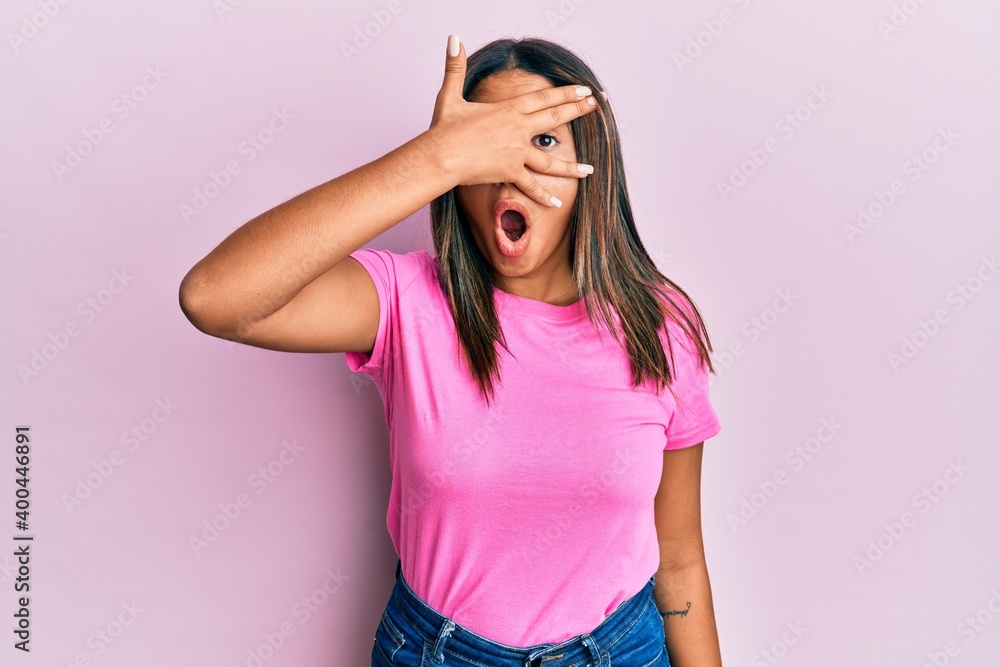 Young latin girl wearing casual clothes peeking in shock covering face and eyes with hand, looking through fingers afraid Young latin girl wearing casual clothes peeking in shock covering face and eyes with hand, looking through fingers afraid