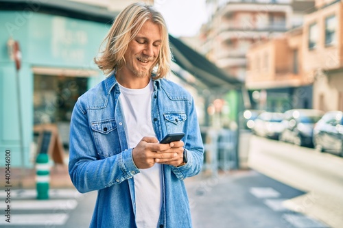Young blond scandinavian man smiling happy using smartphone at the city.