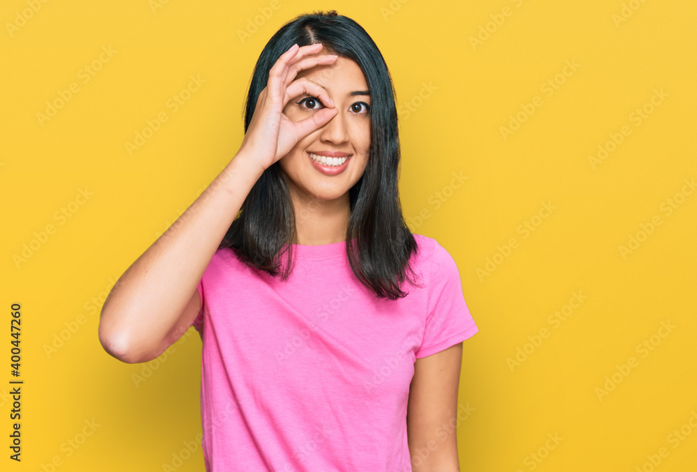 Beautiful asian young woman wearing casual pink t shirt doing ok gesture with hand smiling, eye looking through fingers with happy face. Beautiful asian young woman wearing casual pink t shirt doing ok gesture with hand smiling, eye looking through fingers with happy face.