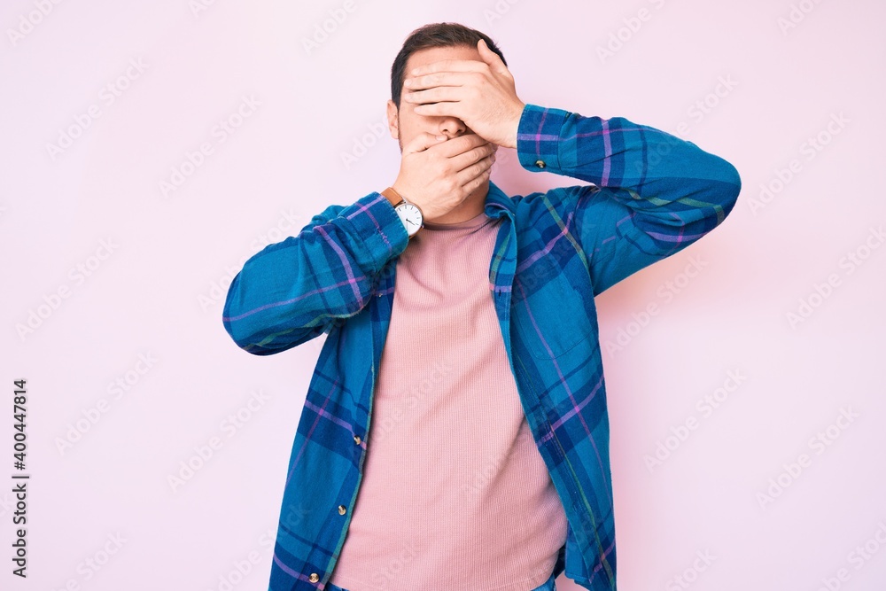 Young handsome man wearing casual clothes covering eyes and mouth with hands, surprised and shocked. hiding emotion Young handsome man wearing casual clothes covering eyes and mouth with hands, surprised and shocked. hiding emotion